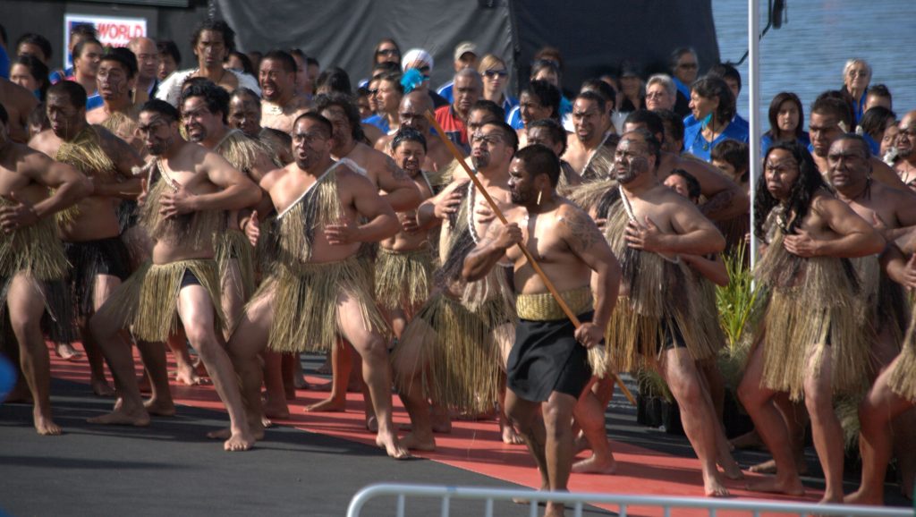 Danseurs maoris executant un haka, yeux ecarquilles et bras tendus